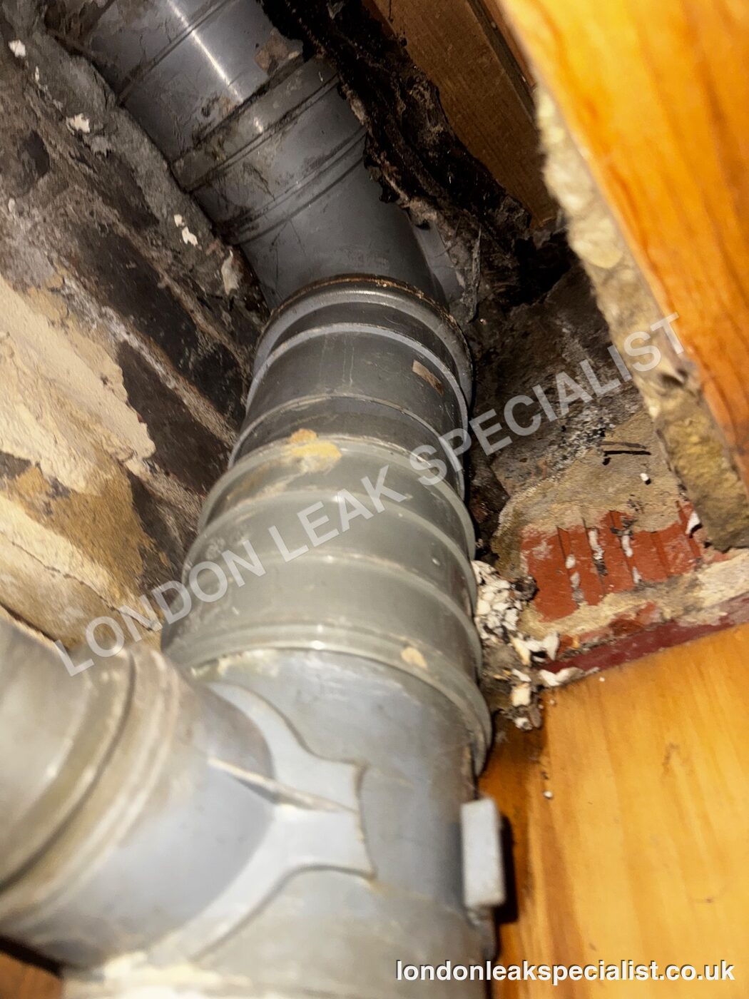 Grey plastic soil pipe with a large bend and joint inside a ceiling void, next to brickwork and timber