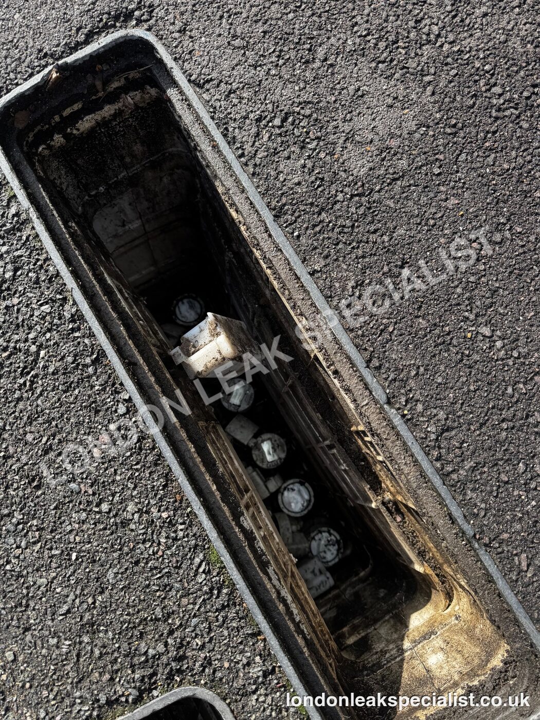 An open external chamber in tarmac showing stop valve fittings at the bottom